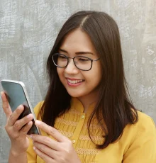 Smiling Asian woman wearing glasses while using a smartphone